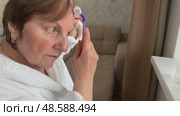 A beautiful senior woman is sitting at home and doing her make-up morning routine. Senior woman putting blush on her face. Стоковое видео, видеограф Ирина Старикова / Фотобанк Лори