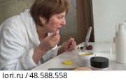A beautiful senior woman is sitting at home and doing her make-up morning routine. Senior woman putting blush on her face. Стоковое видео, видеограф Ирина Старикова / Фотобанк Лори