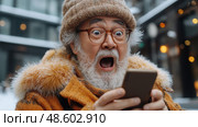 An elderly man is visibly shocked and excited as he looks at his smartphone, dressed warmly for the winter in a snowy city. Стоковое AI-изображение, AI-художник Данила Большаков / Фотобанк Лори