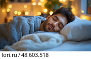 A young man enjoys a restful sleep wrapped in a blanket, surrounded by warm lighting in a tranquil bedroom atmosphere. Стоковое AI-изображение, AI-художник Данила Большаков / Фотобанк Лори