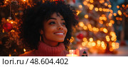 A woman with curly hair smiles contentedly, surrounded by candles and bright Christmas decorations, celebrating the holiday spirit. Стоковое AI-изображение, AI-художник Данила Большаков / Фотобанк Лори