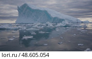 Large iceberg surrounded by drifting ice pieces in a peaceful polar seascape, under a dramatic, cloudy sky during twilight. Majestic Arctic Iceberg Floating in Calm Ocean. Стоковое AI-видео, аниматор Башкирова Анна / Фотобанк Лори