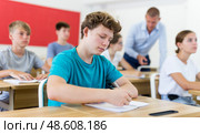 Diligent teenage student making notes of teacher lecture. Стоковое фото, фотограф Яков Филимонов / Фотобанк Лори