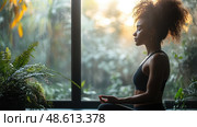 A woman sits quietly in an indoor garden, meditating peacefully as morning sunlight filters through the lush greenery around her. Стоковое AI-изображение, AI-художник Данила Большаков / Фотобанк Лори