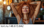 A woman with curly hair smiles contentedly, savoring a peaceful moment in a cozy cafe with warm lighting and a relaxed atmosphere. Стоковое AI-изображение, AI-художник Данила Большаков / Фотобанк Лори