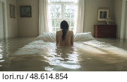 The room is immersed in water as a woman sits quietly on the bed, reflecting the unusual and serene moment in the flooding luminance. Стоковое AI-изображение, AI-художник Данила Большаков / Фотобанк Лори