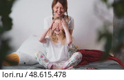 Cheerful woman gently covers her daughters eyes during play on bed. Loving moment full of emotion, care and warmth, representing pure family fun and safety. Стоковое видео, видеограф Енваев Андрей / Фотобанк Лори