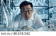 A scientist in a lab coat studies various glass containers meticulously at a laboratory during the night, exploring new scientific breakthroughs. Стоковое AI-изображение, AI-художник Данила Большаков / Фотобанк Лори