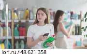 European girl scans a barcode on her mobile for washing dishes against the background of other visitors to the household department of the supermarket. Young woman pays for purchases using a QR code. Стоковое видео, видеограф Яков Филимонов / Фотобанк Лори