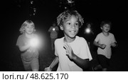 Children running joyfully through a dark forest with flashlights during a summer night adventure. Стоковое AI-изображение, AI-художник Сергей Толмачёв / Фотобанк Лори