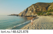 Woman walking barefoot on a quiet sandy beach in Kefalonia during the warm evening light. Стоковое видео, видеограф Igor Tichonow / Фотобанк Лори