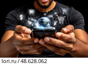 A man is holding a cell phone with a globe and shopping carts on the screen. Стоковое AI-изображение, AI-художник Ярославский Максим / Фотобанк Лори