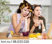 Female friends applying sheet masks to faces by vanity mirror. Стоковое фото, фотограф Яков Филимонов / Фотобанк Лори