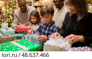Family gathers around tree to unwrap gifts during Christmas celebration in a warm and festive atmosphere. Стоковое AI-изображение, AI-художник Сергей Толмачёв / Фотобанк Лори