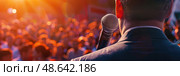The speaker passionately engages a captivated audience at sunset, holding a microphone, as attendees eagerly listen and participate. Стоковое AI-изображение, AI-художник Данила Большаков / Фотобанк Лори