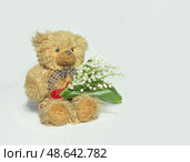 Мишка Тедди, держит в руках ландыши, крупным планом, на изолированном фоне. Teddy bear holding lilies of the valley, close-up, on isolated background. Редакционное фото, фотограф Наталья Пеньшина / Фотобанк Лори