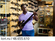 African american man chooses rifle with telescopic sight and silencer. Стоковое фото, фотограф Яков Филимонов / Фотобанк Лори