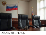 В зале заседаний суда стоят три кресла, а на столе расположен микрофон. На стене виден флаг России, символизирующий правосудие и закон. Стоковое AI-изображение, AI-художник Сергей Никифоров-Гордеев / Фотобанк Лори