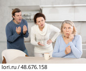 Woman and man swear at old mother who puts up with it while sitting at kitchen table. Стоковое фото, фотограф Яков Филимонов / Фотобанк Лори