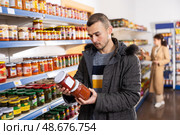 In Russian goods store, man choose jar of canned lecho. Стоковое фото, фотограф Яков Филимонов / Фотобанк Лори