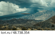A flying saucer floats in the sky above mountains, complementing the dark, stormy atmosphere and rocky terrain. Стоковое AI-изображение, AI-художник Данила Большаков / Фотобанк Лори