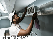 Maintenance worker adjusts air vent in modern basement room during the afternoon. Стоковое фото, фотограф Сергей Толмачёв / Фотобанк Лори