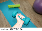 Гантель в женской руке на фоне фитнес-коврика, фитбола и рола в комнате. Упражнение для мышц рук. Стоковое фото, фотограф Юлия Королева / Фотобанк Лори
