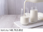 Pouring homemade kefir, buttermilk or yogurt with probiotics. Yogurt flowing from glass bottle on light background. Probiotic cold fermented dairy drink. Trendy food and drink. Copy space. Стоковое фото, фотограф Наталия Попова / Фотобанк Лори