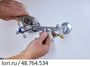 Unscrewing old two handle faucet from wall, hands use wrench to loosen fixture with visible signs of wear, central opening remains without spout. Стоковое фото, фотограф Владимир Григорьев / Фотобанк Лори