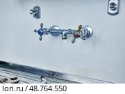 Faucet with blue and red handles is mounted on white wall above metal sink, spout is detached and lying on sink, surfaces show signs of use. Стоковое фото, фотограф Владимир Григорьев / Фотобанк Лори