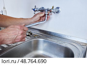 Removing faucet spout from wall-mounted tap by hand in preparation for replacement using visible plumbing tools placed near kitchen sink. Стоковое фото, фотограф Владимир Григорьев / Фотобанк Лори