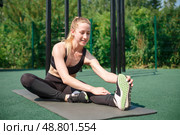 A beautiful athletic young woman is engaged in outdoor fitness in the summer. A sporty woman stretches and warms up in the sports arena. An attractive young woman does a stretch before fitness. Стоковое фото, фотограф Иван Карпов / Фотобанк Лори