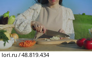 The cook cuts white onions into thin slices on a wooden cutting board in a rustic manner while preparing a snack outdoors. Стоковое видео, видеограф Strunov David / Фотобанк Лори
