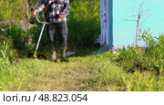 Gardener with grass trimmer mows lawn. Стоковое видео, видеограф Igor Skripachev / Фотобанк Лори