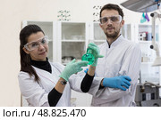Two chemists work in a modern chemical laboratory. Senior chemist and laboratory assistant study the green solution in the flask. Стоковое фото, фотограф Регина Ерофеева / Фотобанк Лори