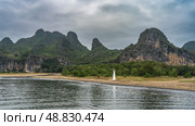 Beautiful calm river. Ripples on the shiny water. There is a lighthouse on the shore, green vegetation. Picturesque mountains against the sky and clouds. China. Li River. Li Jiang. Guilin. Стоковое фото, фотограф Вера Ивановна Кубарева / Фотобанк Лори