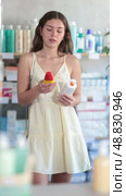 Woman in a summer dress stands near the counter in a pharmacy and chooses a sunscreen and SPF to protect the skin. Стоковое видео, видеограф Яков Филимонов / Фотобанк Лори