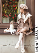 Vintage accessories and retro-style clothes. A small, beautiful girl with bows in her hair, in a beige dress and a beret outdoors with bagels and milk in a string bag. Стоковое фото, фотограф Photojuli / Фотобанк Лори