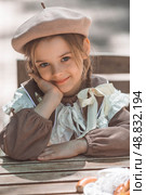 Vintage women's accessories and retro-style clothing. A small, beautiful girl with bows in her hair, in a beige dress and a beret outdoors. Стоковое фото, фотограф Photojuli / Фотобанк Лори