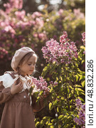 Vintage women's accessories and retro-style clothing. A small, beautiful girl with bows in her hair, in a beige dress and a beret outdoors. Стоковое фото, фотограф Photojuli / Фотобанк Лори