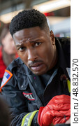A close-up portrait of a male firefighter wearing a black jacket and red gloves, focused intently during an emergency response. Стоковое AI-изображение, AI-художник Данила Большаков / Фотобанк Лори