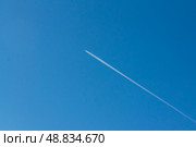 A plane leaves a white contrail across the clear blue sky, a sign of travel and distant journeys. Against the serene blue sky, a jet streaks, its contrail a fleeting mark of human passage, connecting distant places and leaving a temporary imprint on the vastness of the atmosphere. Стоковое фото, фотограф Андрей Ка / Фотобанк Лори