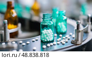 Bottles filled with white pills on production line in a pharmaceutical facility during daytime. Стоковое AI-изображение, AI-художник Сергей Толмачёв / Фотобанк Лори