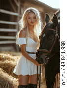A blonde woman is posing with a black horse in a field. Стоковое AI-изображение, AI-художник Ярославский Максим / Фотобанк Лори