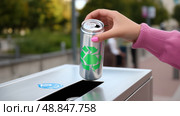 Hand dropping a recyclables can into a recycling bin on a sunny day in an urban park area near trees and people. Стоковое AI-изображение, AI-художник Сергей Толмачёв / Фотобанк Лори