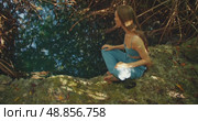 Woman sits barefoot at the edge of a quiet mangrove lagoon or cenote with clear fresh water. Стоковое видео, видеограф Igor Tichonow / Фотобанк Лори