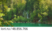 Plitvice waterfall cascades down mossy rocks into blue lake in Croatia during summertime visit. Стоковое видео, видеограф Igor Tichonow / Фотобанк Лори