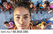 A young woman looks into the camera surrounded by a diverse group of people participating in an outdoor exercise session. Стоковое AI-изображение, AI-художник Данила Большаков / Фотобанк Лори
