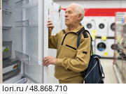 Senor man pensioner buying fridge in showroom of electrical appliance store. Стоковое фото, фотограф Татьяна Яцевич / Фотобанк Лори