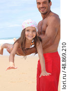 little girl lying down on father&rsquo;s arms on the beach. Стоковое фото, агентство Ingram Publishing / Фотобанк Лори